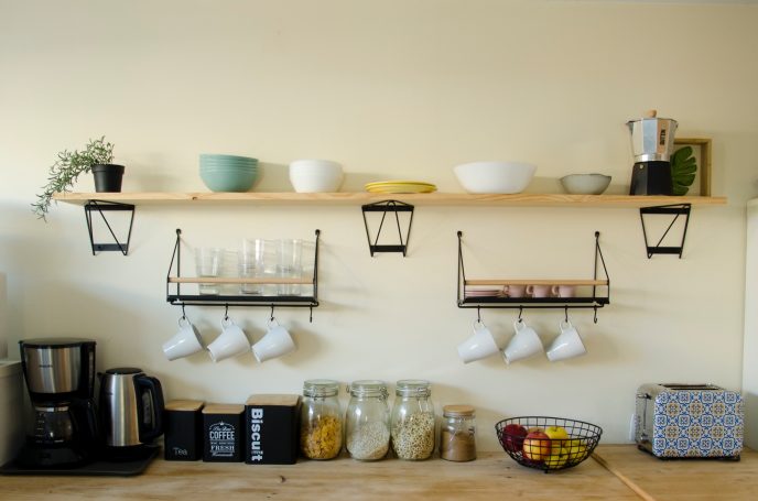 Estantería de cocina con utensilios, vasos, tazas y una batidora sobre una mesa.